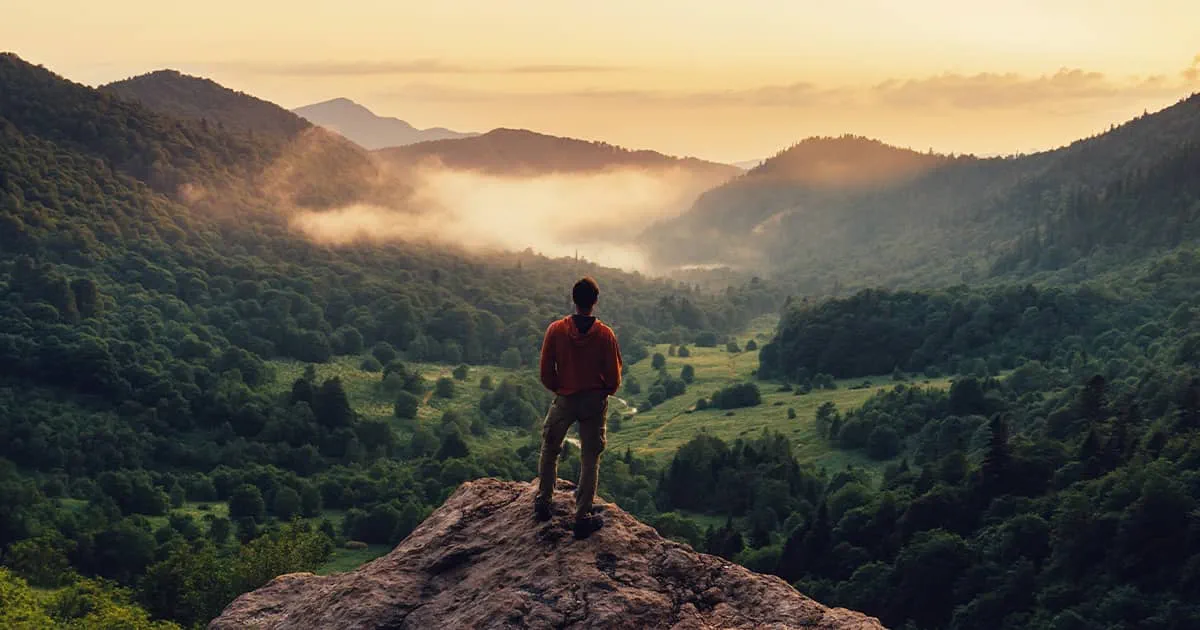 Man exploring and standing on top of cliff at sunset